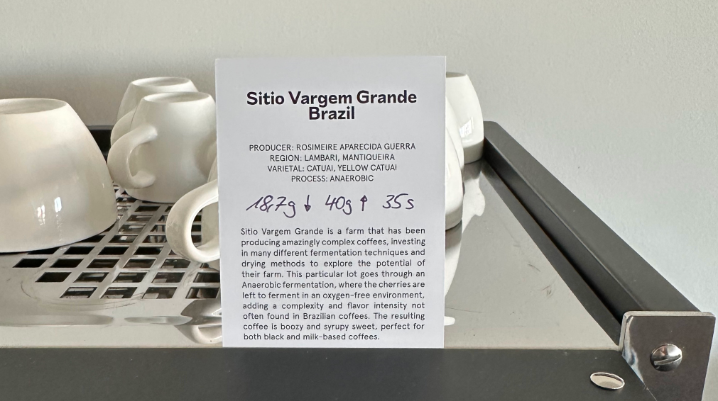 A coffee recipe wirtten onto a piece of paper which is stuck to the top of a espresso machine