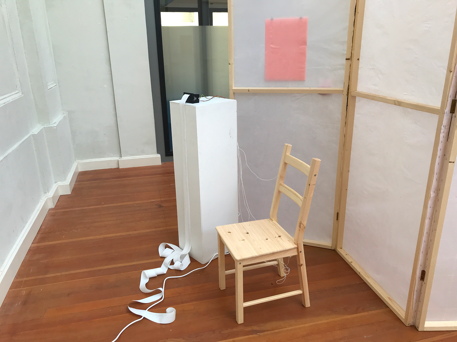 Wooden chair connected to a reciept printer standing next to it which prints an endless piece of paper