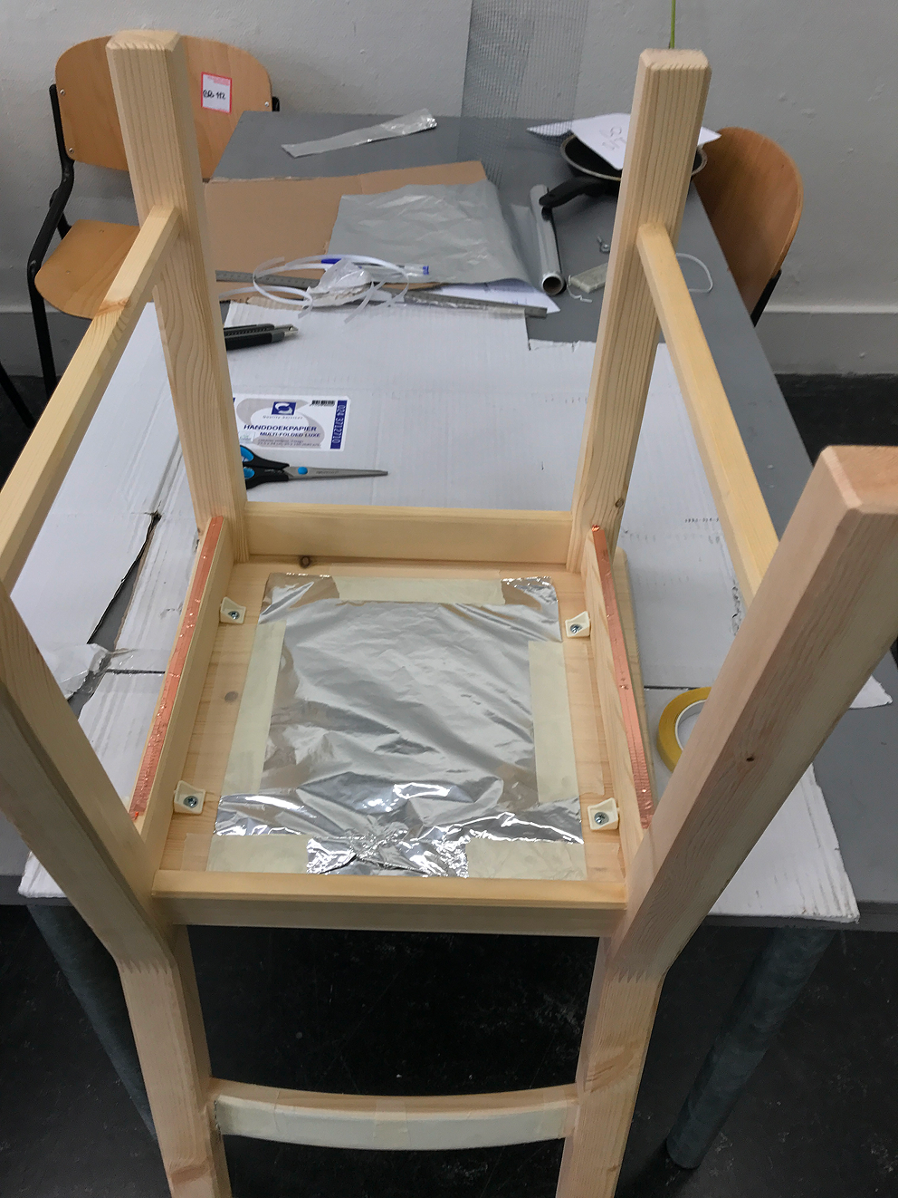 A wooden chair upside down on a table with aluminum foil glued to the bottom of the chair