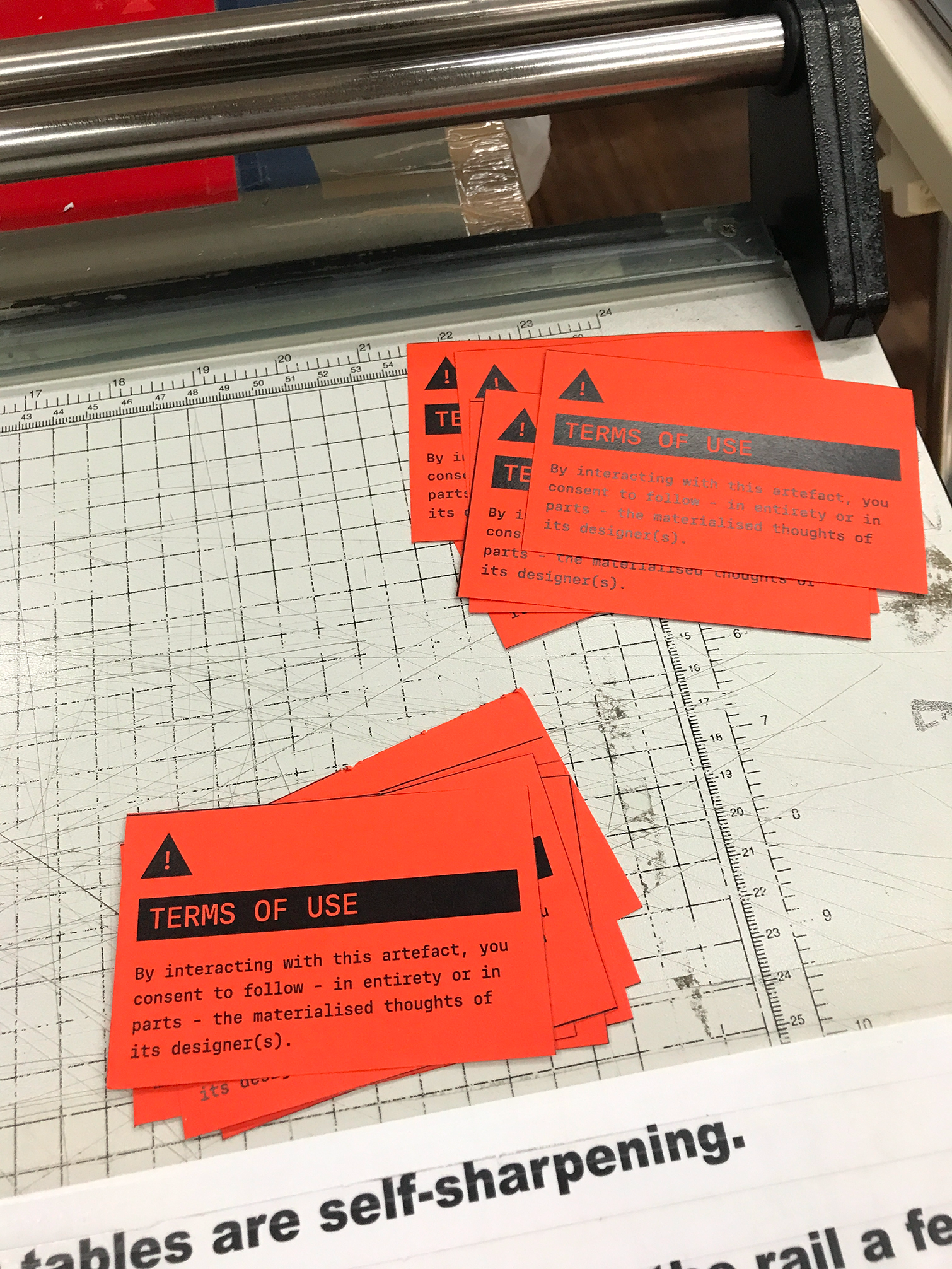 Photo of a set of bright orange stickers with the text 'Terms of Use. By interacting with this artifact, you consent to follow – in entirety or in parts – the materialized thoughts of its designer(s)'